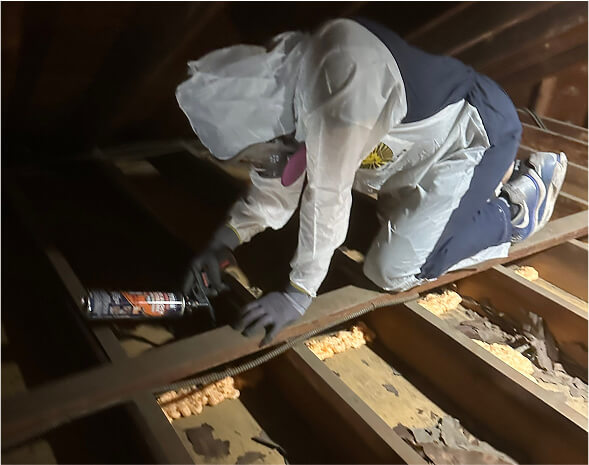 A person sealing air gaps in an attic kneeling on rafters