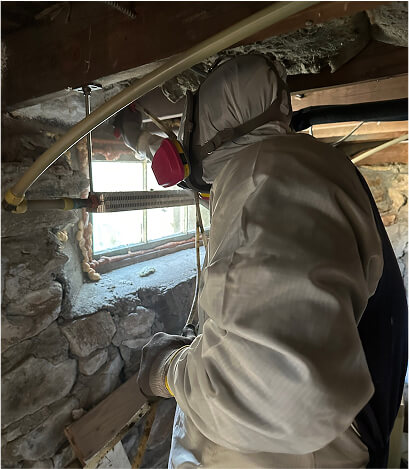 Individual in full protective suit sealing air gaps in a basement