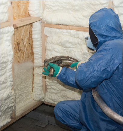 Person covered in protective suit spraying foam on a wall frame