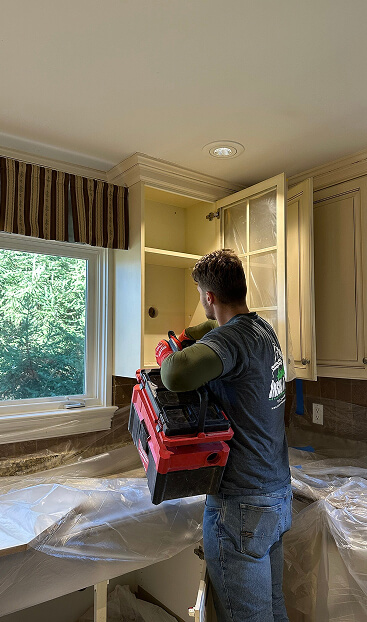 Man injecting insulation into wall through the back of a kitchen cupboard